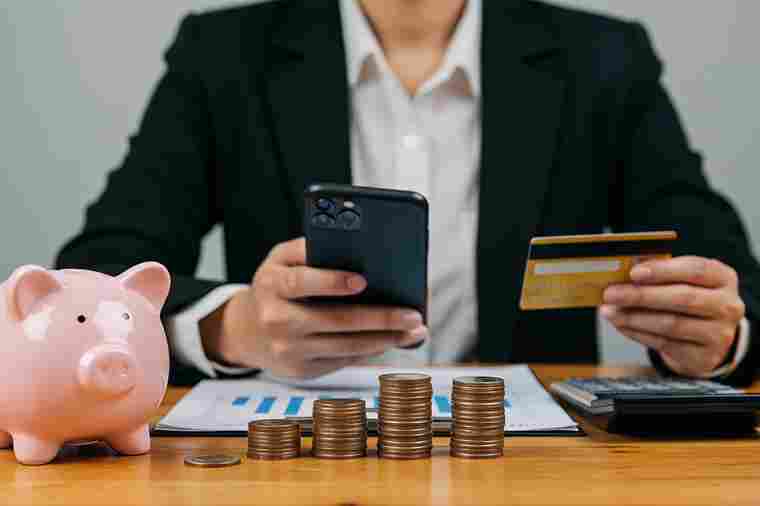 © Sultan - stock.adobe.com Mann mit Smartphone, Bankomatkarte, Sparschwein und Münzen